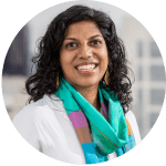 Portrait of a smiling woman with dark curly hair wearing a colorful scarf and white blouse.