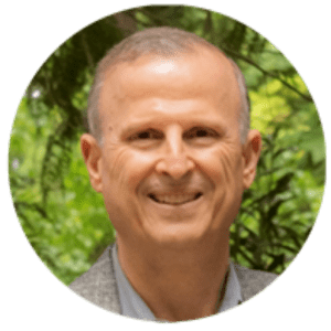 Smiling middle-aged man photographed outdoors with green foliage in the background, circular crop.