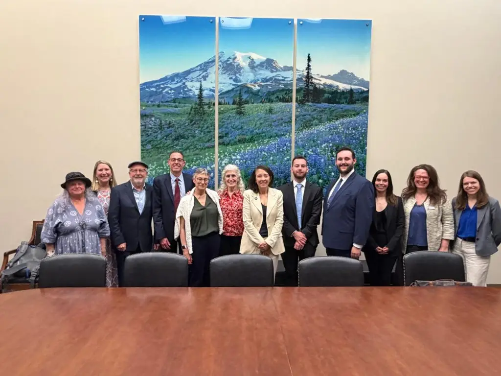 Group of twelve people in business and casual attire posing for a photo in a conference room with a three-panel mountain landscape painting behind them.