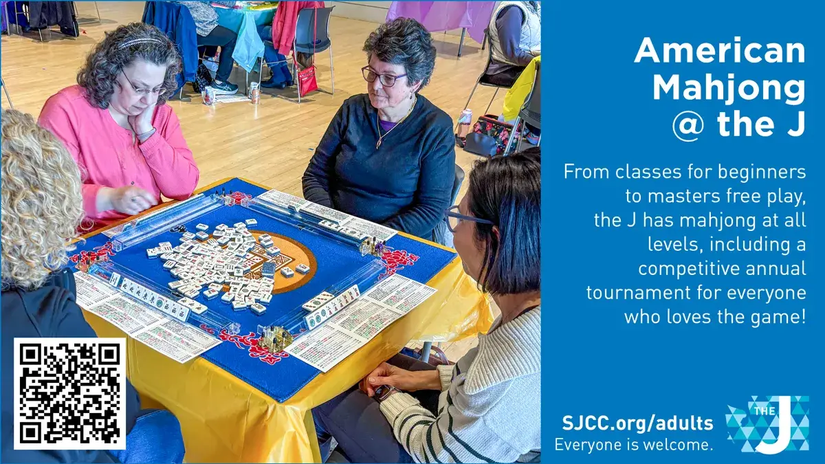 Four players sit around a mahjong table with tiles and score sheets; a blue promotional panel on the right reads 'American Mahjong @ the J' with a QR code in the bottom-left corner.