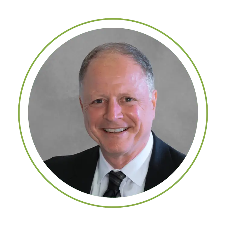 Smiling man in a dark suit and tie, professional headshot against a gray background with a green circular frame.