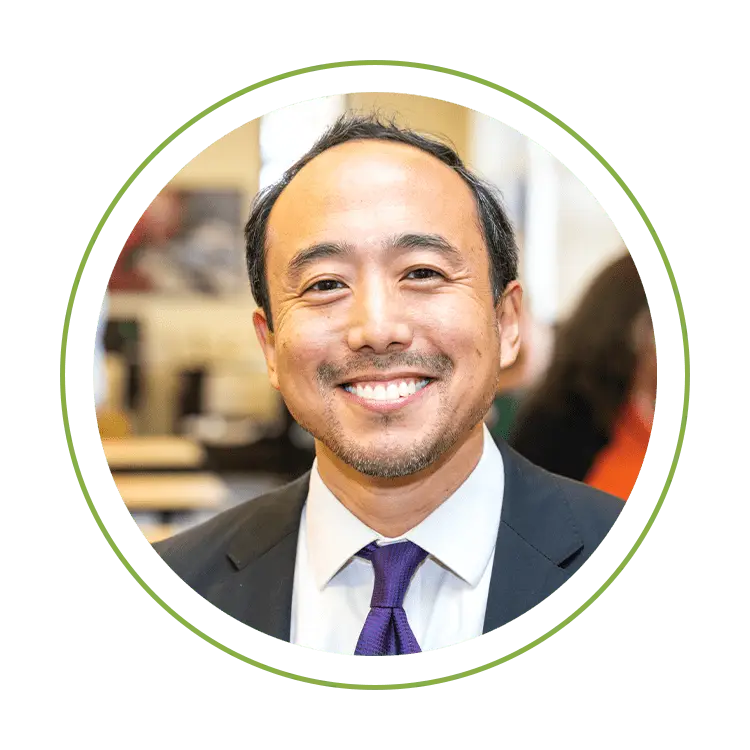 Smiling man in a suit with a purple tie, circular crop on a green background