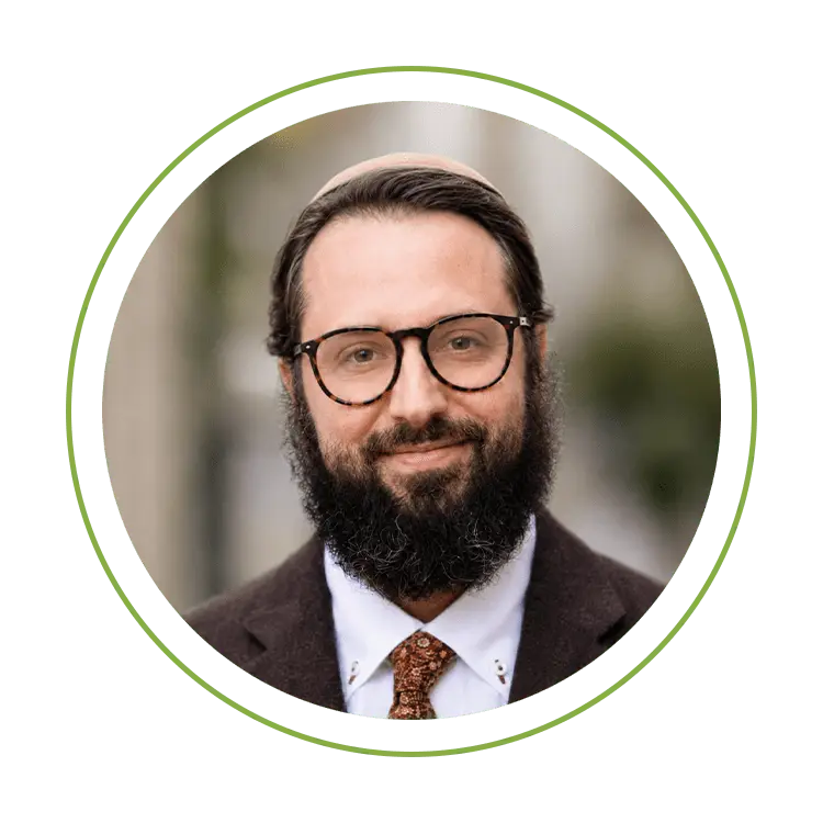 Portrait of a bearded man with glasses, wearing a brown blazer, white shirt, and patterned tie, smiling at the camera.