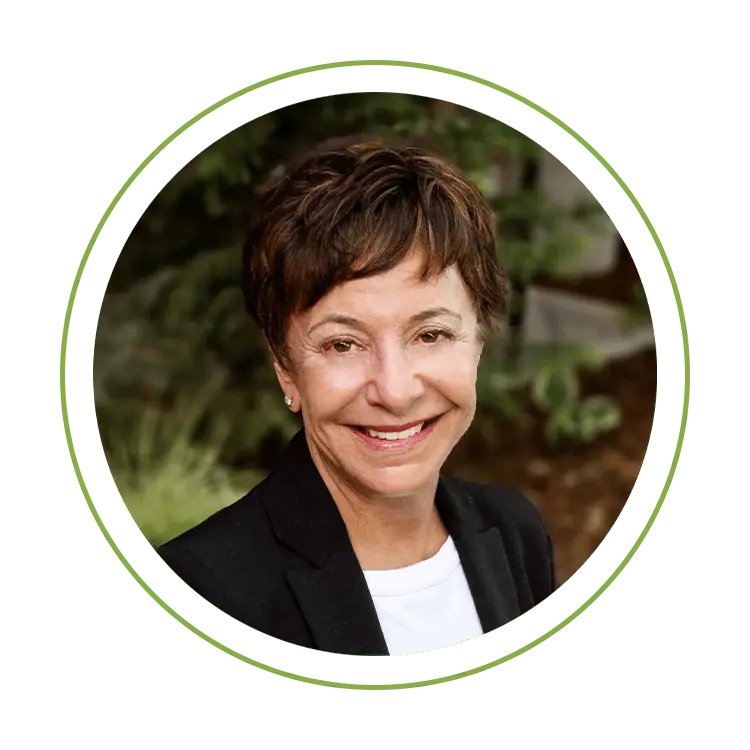 Smiling woman in a black blazer and white shirt, portrait photo inside a green circular frame.