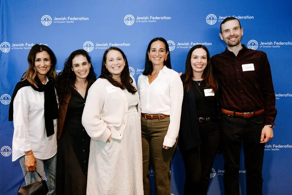 Six adults posing together for a group photo in front of a blue backdrop with the Jewish Federation of Greater Seattle logo(s).
