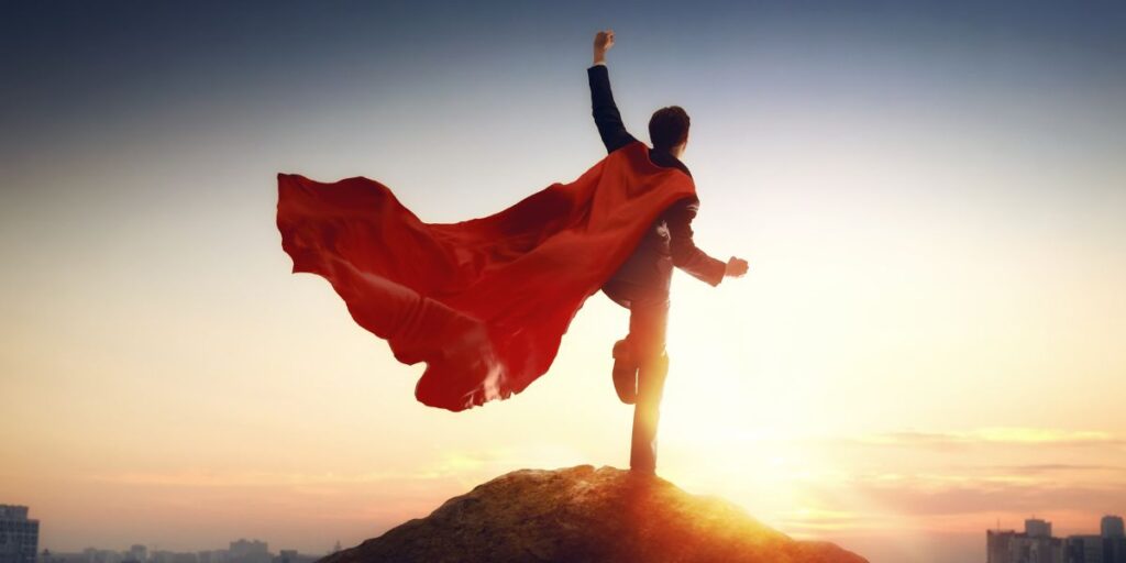 Person on a rocky peak with a flowing red cape at sunrise, symbolizing triumph and empowerment Free to consent.