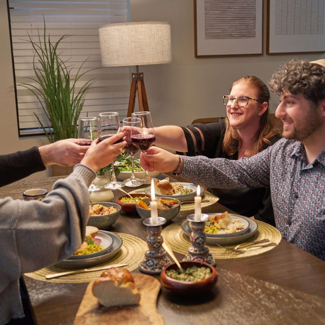 A group of friends toast at a shabbat dinner table