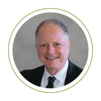 Smiling man in a dark suit and tie, professional headshot against a gray background with a green circular frame.