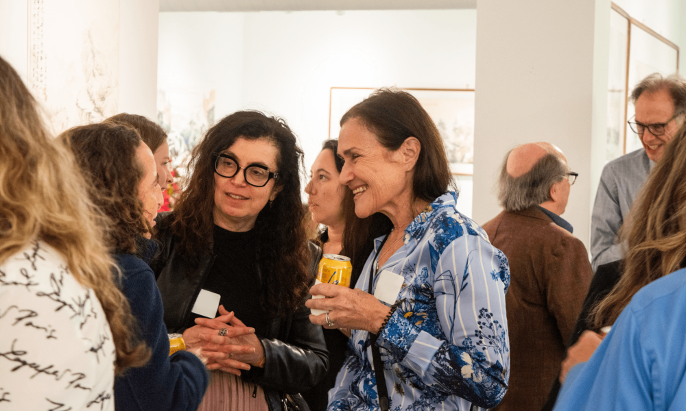 Group of people chatting at an art gallery, holding drinks and smiling.