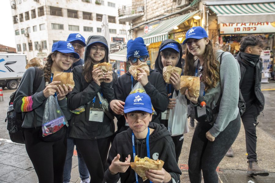 Group of smiling young volunteers in blue caps eating hot dogs at an outdoor market festival