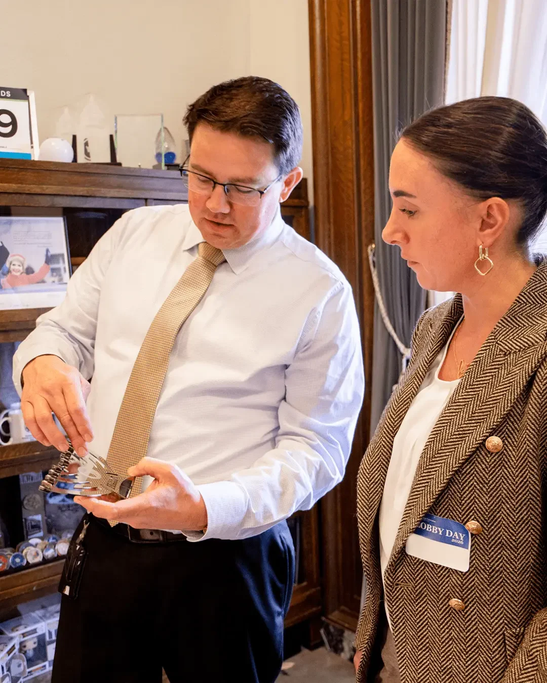 Two professionals examine a metal object together in an office, the man showing details to the woman beside him.