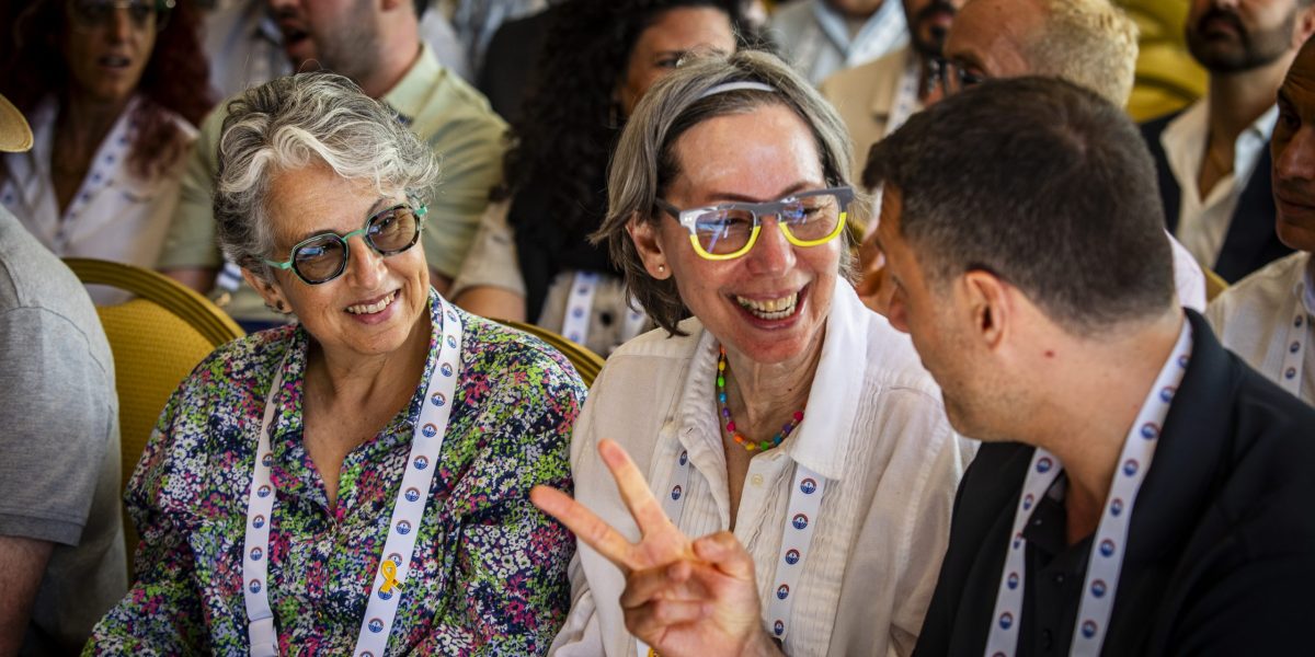 Smiling group of diverse people at a conference, foreground two women with lanyards and colorful clothing.